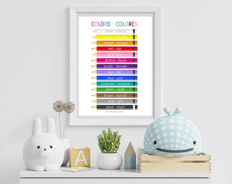 Op de afbeelding: Een afdrukbare poster met een witte achtergrond en kleurpotloden. De poster toont de namen van kleuren in het Engels en Spaans. De tekst luidt "COLORS - COLORES" en "Let's go to learn!"