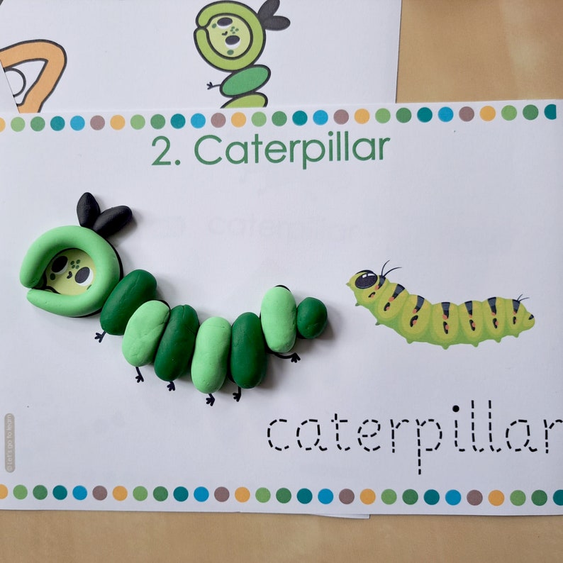 May include: A green caterpillar made of play dough with a black head and legs. The word "caterpillar" is written in dotted lines below the caterpillar.