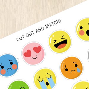 Op de afbeelding: Een printbare set van negen kleurrijke emoji-gezichten met verschillende uitdrukkingen. De tekst "CUT OUT AND MATCH!" staat bovenaan de pagina.