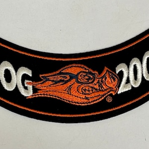 May include: Black and orange embroidered patch with the word "HOG" in white lettering and a cartoon pig wearing sunglasses. The year "2006" is also embroidered in white lettering.