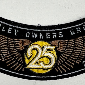 Könnte beinhalten: Schwarzer Harley Owners Group Patch mit braunen gestickten Flügeln und dem Text "Harley Owners Group" und "1983 2008" um einen gelben Kreis mit der Zahl "25" in Weiß.