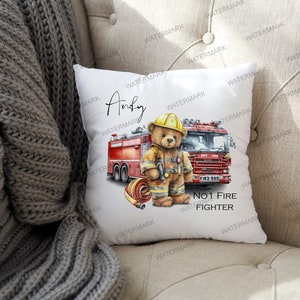 May include: A white cushion featuring a red fire engine and a teddy bear dressed in a firefighter's outfit. The text "Andy" and "No. 1 Fire Fighter" is printed on the cushion.