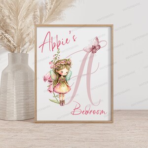 May include: A pink and white watercolour illustration of a fairy with wings and a flower crown. The fairy is standing in front of a large pink letter A with the text "Abbie's Bedroom" below.