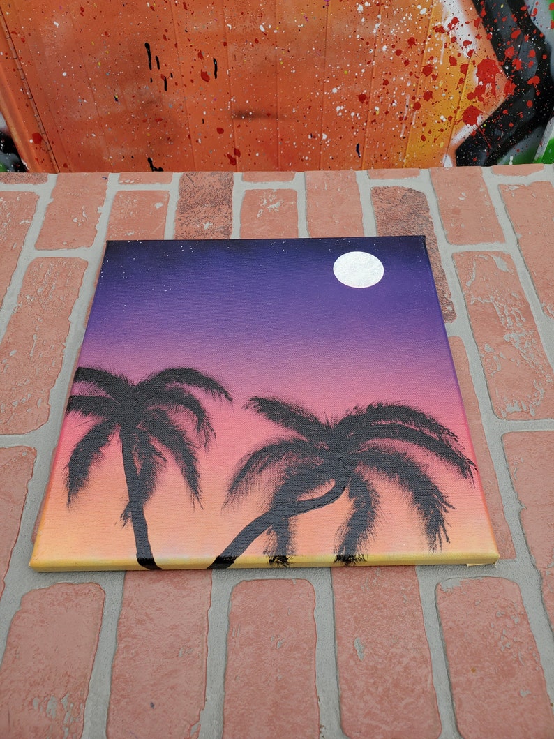 May include: A painting of a sunset with two palm trees and a full moon in the sky. The sky is a gradient of purple, pink, and orange. The palm trees are black silhouettes against the sunset.