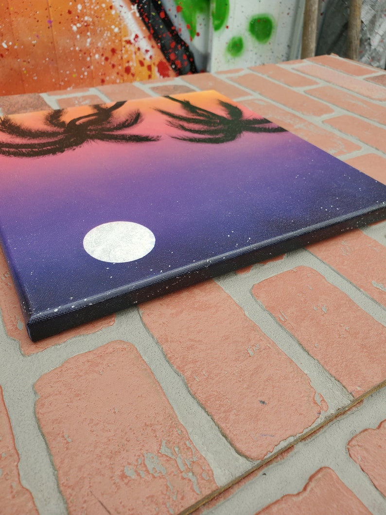 May include: A painting on canvas depicting a sunset with palm trees silhouetted against a purple and orange sky. A white moon is visible in the sky.