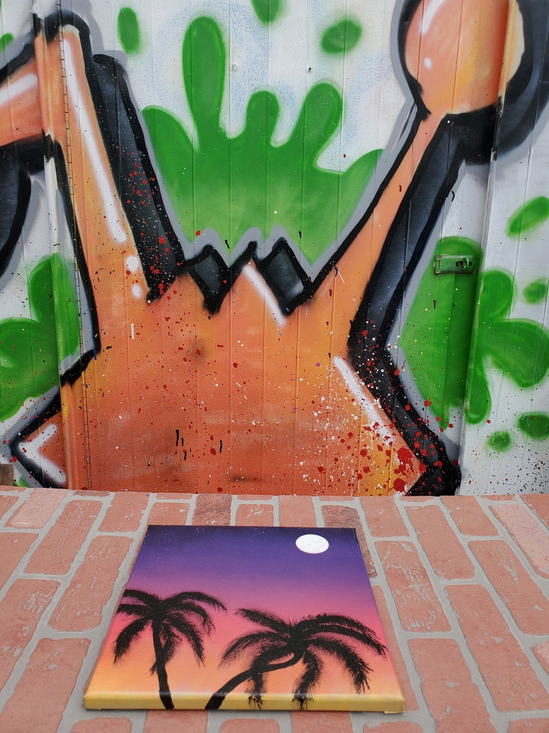 May include: A hand-painted canvas with a sunset scene featuring two palm trees and a full moon. The background is a gradient of purple, pink, and orange.