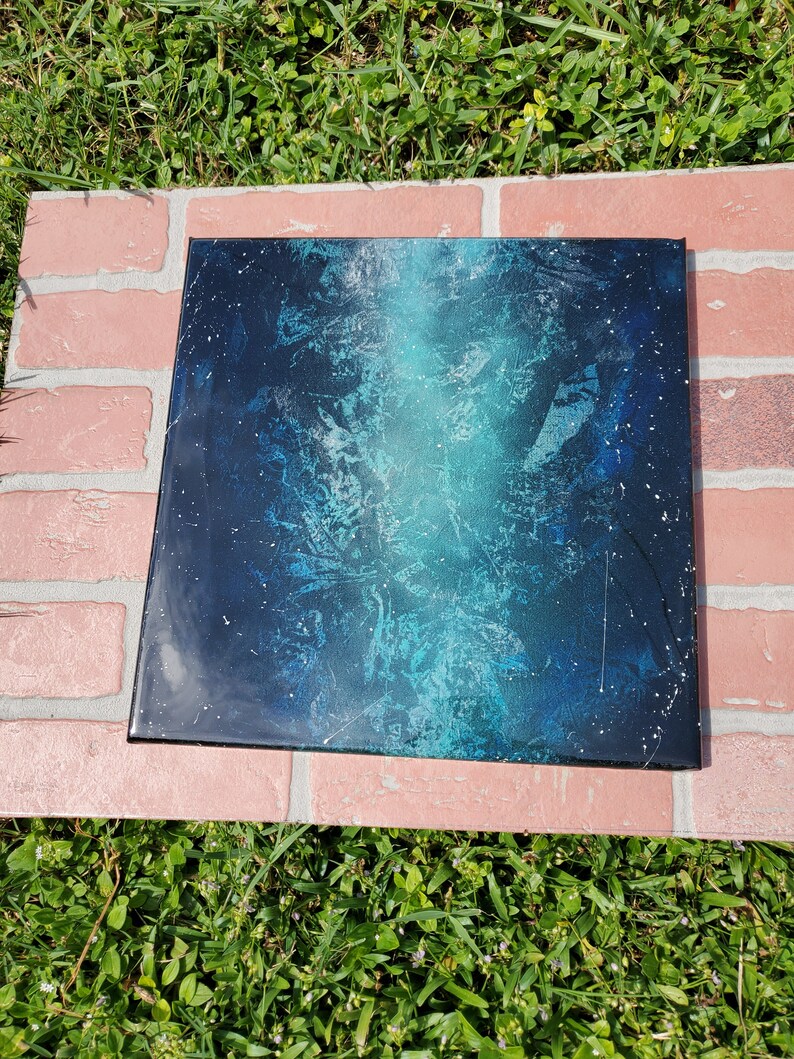 May include: A square canvas painting with a blue and black abstract design. The painting has a white splatter effect and a light blue gradient.
