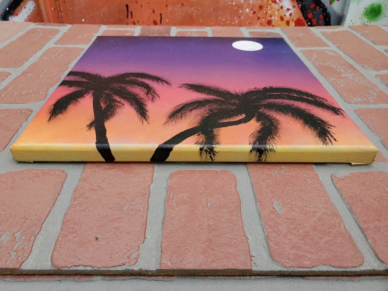 May include: A painting of two palm trees silhouetted against a sunset sky with a full moon. The sky is a gradient of orange, pink, and purple.