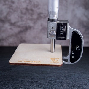 Micrometer measuring a sample of 1/8 inch Baltic birch plywood. Micrometer showing 0.123.