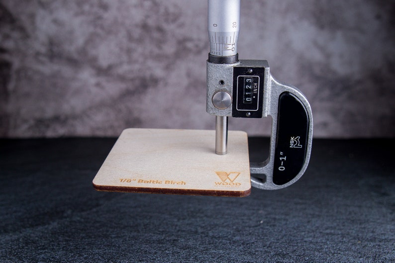Micrometer measuring a sample of 1/8 inch Baltic birch plywood. Micrometer showing 0.123.