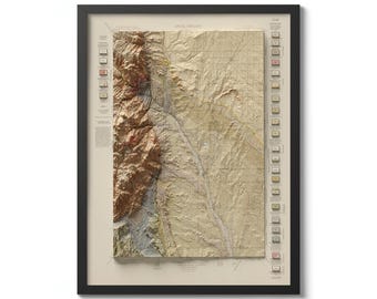 May include: A framed topographic map of a mountainous region with a river running through it. The map is in shades of brown, green, and blue, and it has a grid pattern. The map is titled "ARIAL VIEW" and has a legend on the right side.