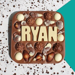 May include: A brown chocolate bar with a white chocolate design of seashells and the name "RYAN" in white chocolate letters.