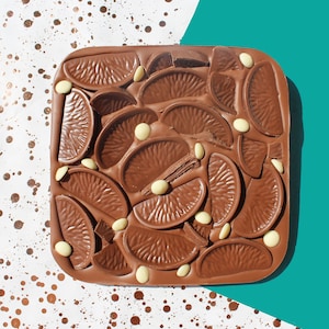 May include: A chocolate bar with a brown chocolate base and white chocolate pieces shaped like orange slices. The chocolate bar is decorated with white chocolate chips.