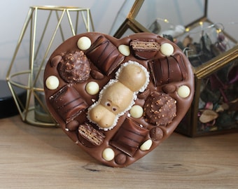 Könnte beinhalten: Eine herzförmige Schokoladentafel mit verschiedenen Belägen, darunter Schokoladenstücke, weiße Schokoladenstückchen und ein hippopotamusförmiges Schokoladenstück.