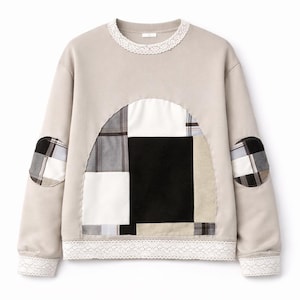Peut inclure: Un sweat-shirt beige à manches longues avec un panneau central en arc orné d'un motif patchwork à carreaux noir, blanc et gris. Le vêtement présente une bordure en dentelle blanche au col, à l'ourlet et aux poignets, avec des coudières rondes assorties.