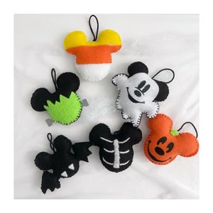 May include: Six felt Halloween ornaments shaped like Mickey Mouse. The ornaments are decorated with different Halloween themes, including a ghost, a pumpkin, a skeleton, a candy corn, and a monster.