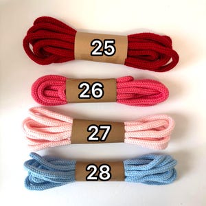 May include: Four bundles of colorful rope, each wrapped with a brown paper band and a number. The colors are red, pink, light pink, and blue. The numbers on the bands are 25, 26, 27, and 28.