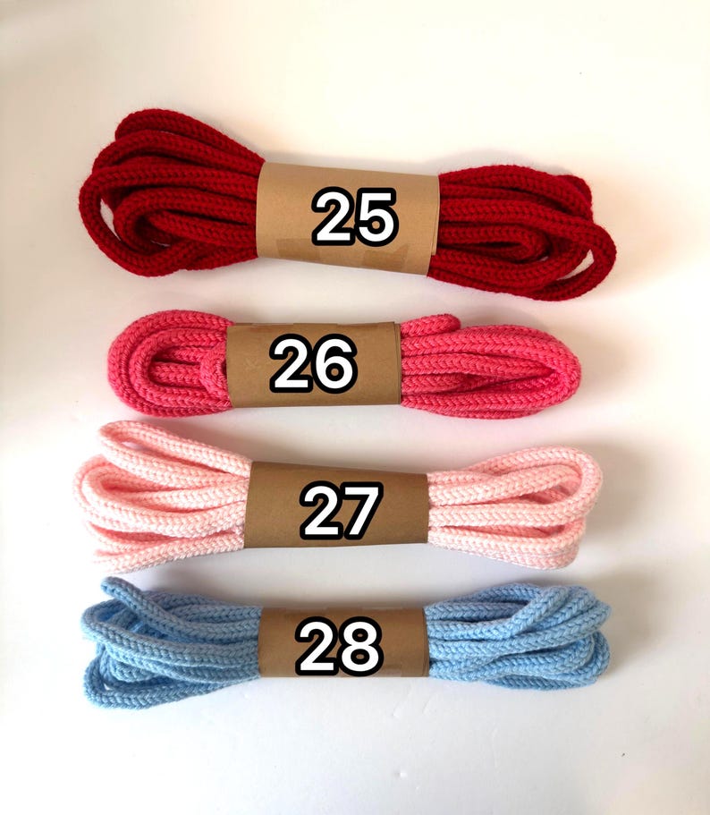 May include: Four bundles of colorful rope, each wrapped with a brown paper band and a number. The colors are red, pink, light pink, and blue. The numbers on the bands are 25, 26, 27, and 28.