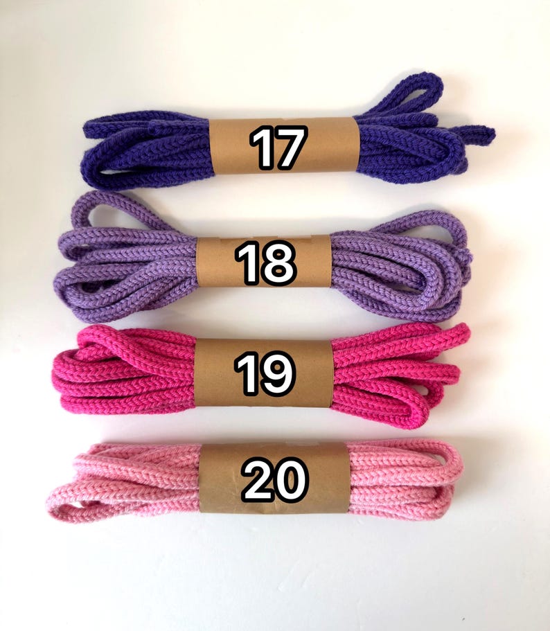 May include: Four sets of braided shoelaces arranged horizontally. The top lace is dark purple labeled 17, followed by a lavender lace labeled 18, a hot pink lace labeled 19, and a light pink lace labeled 20. Each lace is secured with a tan paper band.