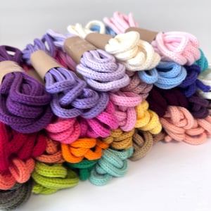 May include: A collection of colorful, braided cords in various hues, including purple, pink, orange, and green. The cords are bundled and wrapped with brown paper. The cords are likely used for crafting or decorative purposes.