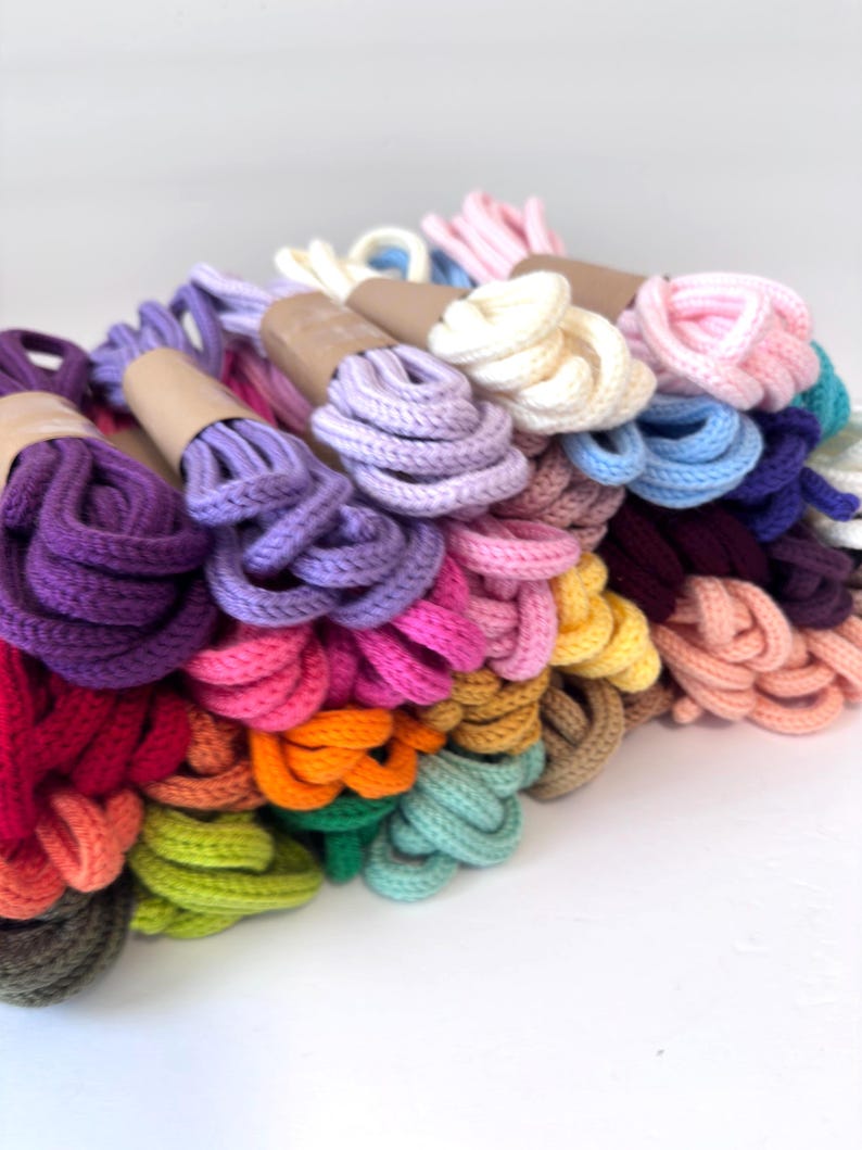 May include: A collection of colorful, braided cords in various hues, including purple, pink, orange, and green. The cords are bundled and wrapped with brown paper. The cords are likely used for crafting or decorative purposes.