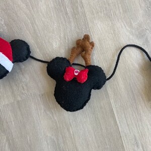 May include: A black felt Christmas garland with a red bow and brown felt reindeer antlers. The garland is strung together with black twine.