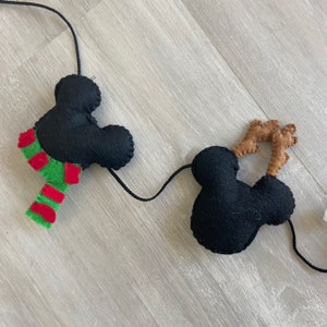 May include: A black felt garland with two Mickey Mouse heads and one Mickey Mouse head with brown antlers. The garland is strung with black thread.