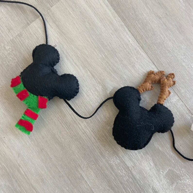 May include: A black felt garland with two Mickey Mouse heads and one Mickey Mouse head with brown antlers. The garland is strung with black thread.