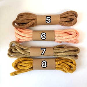 May include: Four bundles of rope in various colors: brown, peach, tan, and mustard yellow. Each bundle is wrapped with a brown paper band and labeled with a number from 5 to 8. The rope appears to be made of a woven material.
