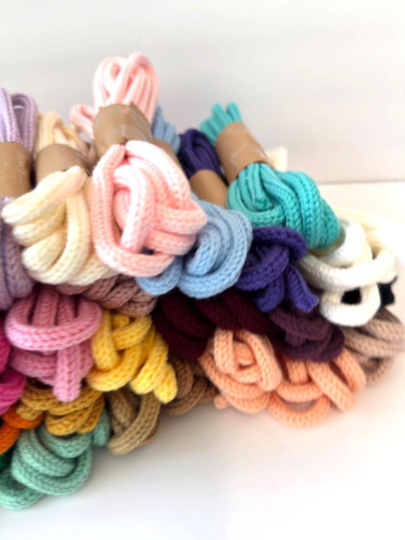 May include: A collection of colorful knitted cords in various shades, including pink, blue, yellow, and green. The cords are bundled and wrapped with brown paper. The image showcases a variety of colors and textures, suitable for crafting or decorative purposes.