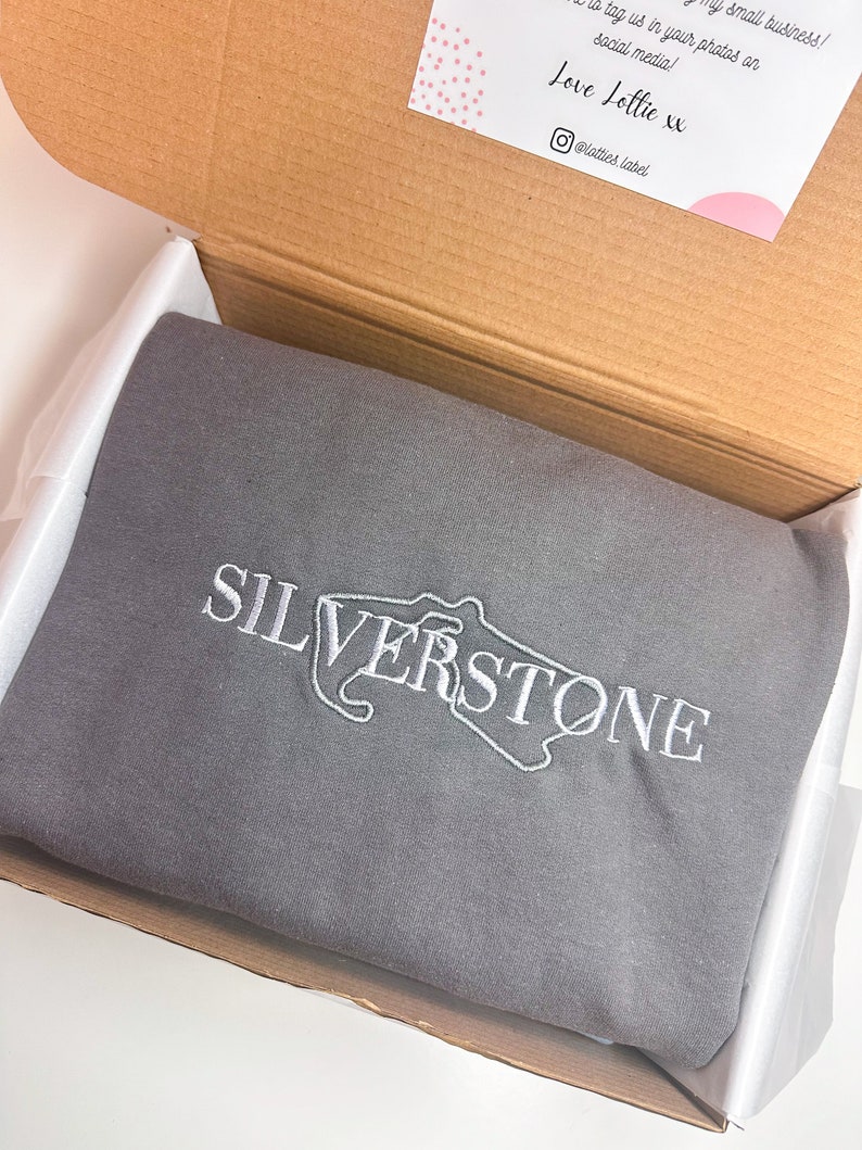 Puede incluir: Una sudadera gris con un dise&ntilde;o bordado en blanco del circuito de Silverstone y la palabra "SILVERSTONE".