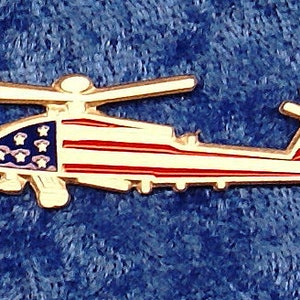 May include: A gold-colored pin of a helicopter with the American flag painted on it. The helicopter is in flight with the blades spinning.