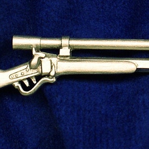 May include: A silver-colored rifle with a scope attached. The rifle has a wooden stock and a metal barrel.