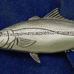 May include: A silver-colored pewter fish figurine. The fish is detailed with scales and fins.