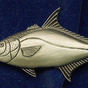 May include: A silver-colored pewter fish figurine. The fish is detailed with scales and fins. The fish is in a side profile position with its mouth slightly open.