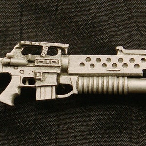 May include: A silver-colored metal replica of a rifle with a barrel, a stock, and a magazine. The rifle has a textured surface and a detailed design.