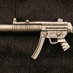 May include: A silver-colored metal replica of a submachine gun. The gun has a black background.