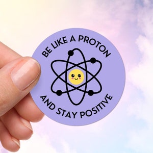 May include: A purple round sticker with a black atom illustration and the text "Be like a proton and stay positive".