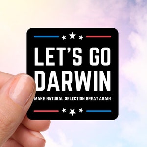 以下が含まれることがあります： 「LET'S GO DARWIN」の白い文字と「MAKE NATURAL SELECTION GREAT AGAIN」のフレーズが書かれた黒い正方形のステッカー。赤と青の線と星のデザイン。