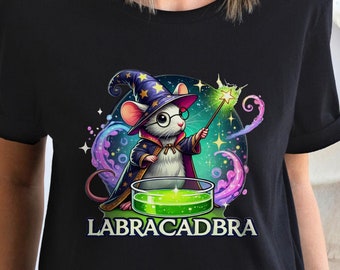 Può includere: T-shirt nera con un topo dei cartoni animati vestito da mago, con cappello e occhiali, che tiene in mano una bacchetta magica. Il topo è circondato da vortici colorati e una pozione verde. Il testo "LABRACADBRA" è stampato sotto.