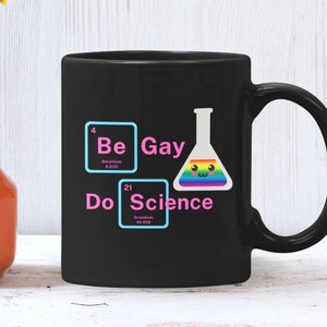 May include: Black coffee mug with a white design featuring the periodic table elements Beryllium (Be) and Scandium (Sc) with the words "Be Gay Do Science". The mug has a rainbow beaker with a cute face.