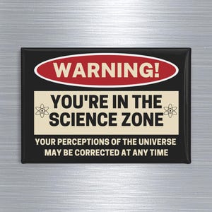 May include: A rectangular black magnet with the text "WARNING! YOU'RE IN THE SCIENCE ZONE" in white and red. The bottom text reads "YOUR PERCEPTIONS OF THE UNIVERSE MAY BE CORRECTED AT ANY TIME."