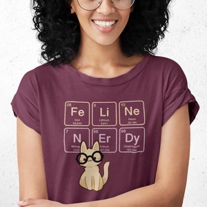 May include: A maroon t-shirt with a graphic of a cat wearing glasses and surrounded by periodic table elements. The elements are Fe, Li, Ne, N, Er, and Dy.