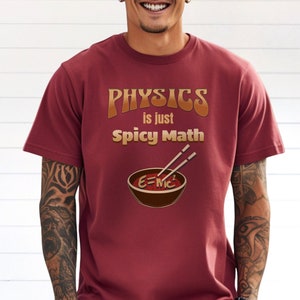 May include: A maroon t-shirt with the text "PHYSICS is just Spicy Math" in a retro font. The design features a bowl of noodles with chopsticks and the equation E=MC2.