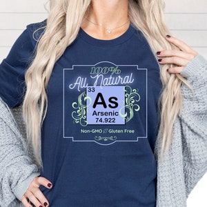 May include: A navy blue t-shirt with a graphic of a periodic table element, arsenic (As), with the text "100% All Natural", "Arsenic", "33", "74.922", "Non-GMO & Gluten Free".