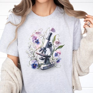 May include: A gray t-shirt with a floral design featuring a microscope and purple and white flowers.