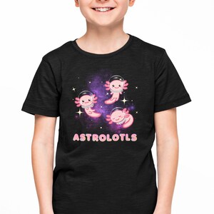 K&ouml;nnte beinhalten: Schwarzes T-Shirt mit einem Galaxie-Druck, auf dem drei rosa Axolotl mit Astronautenhelmen zu sehen sind. Der Text "ASTROLOTLS" ist in rosa und blauen Buchstaben unter den Axolotln gedruckt.