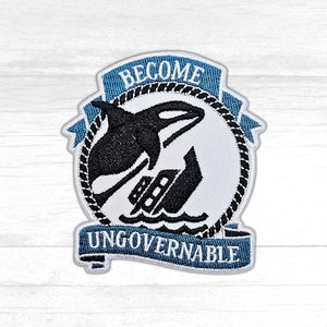 May include: A white and blue embroidered patch with a black orca jumping over a ship. The patch has the text "Become Ungovernable" on a blue banner.