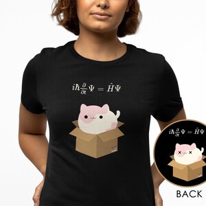 Könnte beinhalten: Schwarzes T-Shirt mit einer Cartoon-Katze in einer Box und der Gleichung ih(∂/∂t)Ψ = ĤΨ darüber gedruckt. Die Katze ist rosa und weiß. Ein kleineres Bild der Katze und der Box befindet sich auf der Rückseite des T-Shirts.