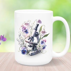 May include: White ceramic mug featuring a floral design with a microscope, pansies, and lily of the valley. The flowers are painted in shades of purple, pink, and white.